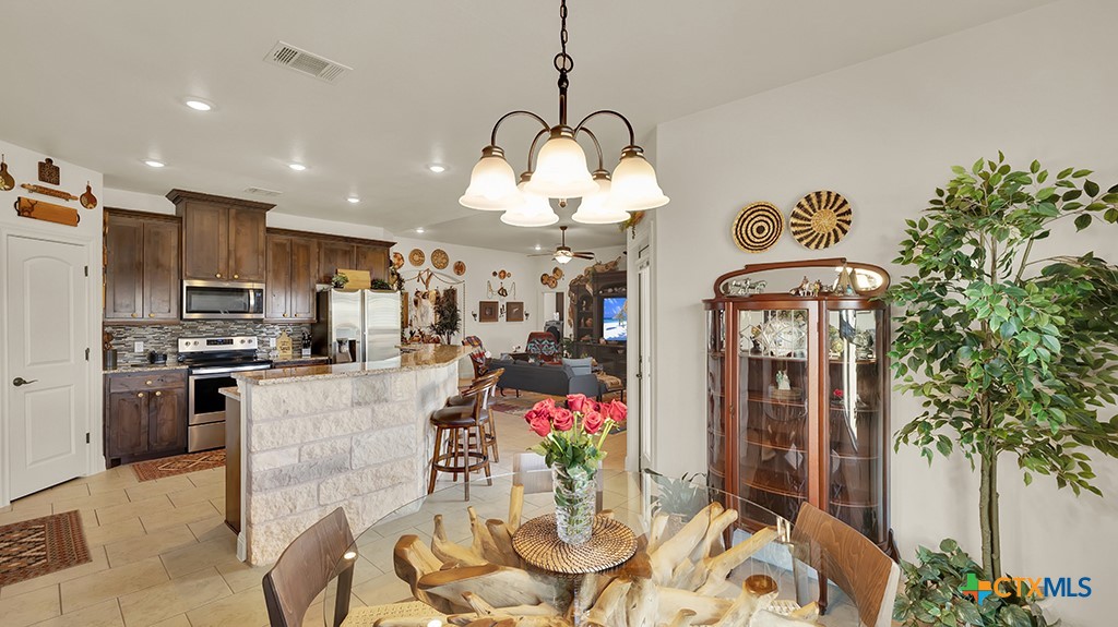 343 Meadow Valley Loop Jarrell, TX 76537 - Photo 24 of 33 a kitchen with stainless steel appliances kitchen island granite countertop a stove a refrigerator a sink a dining table and chairs with wooden floor