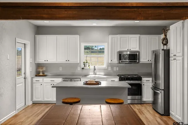 a kitchen with stainless steel appliances granite countertop a refrigerator a stove top oven a sink dishwasher and white cabinets with wooden floor