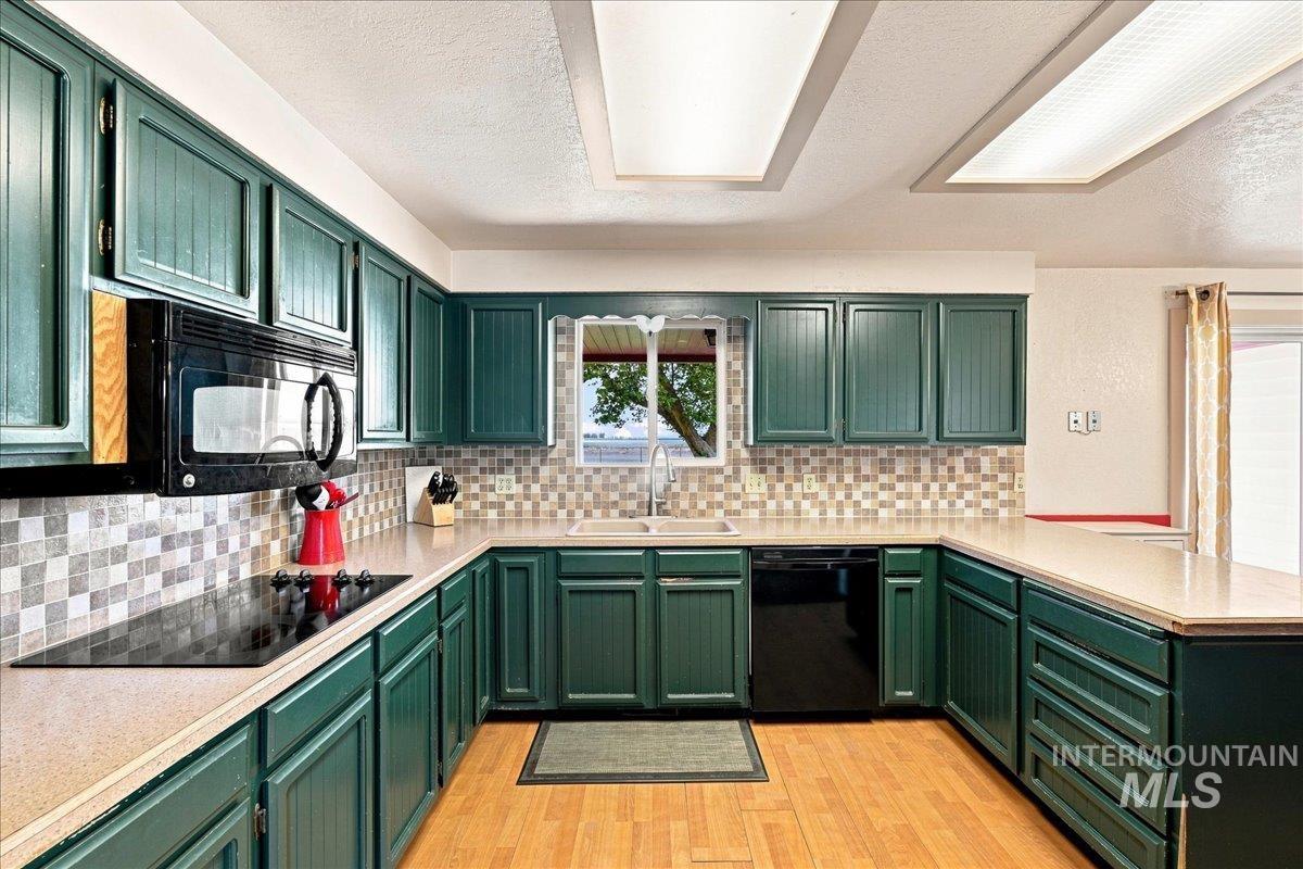 26201 Hop Road Caldwell, ID 83607 - Photo 9 of 45 U-shaped kitchen featuring green cabinetry, light-toned countertops, and a mosaic tile backsplash
