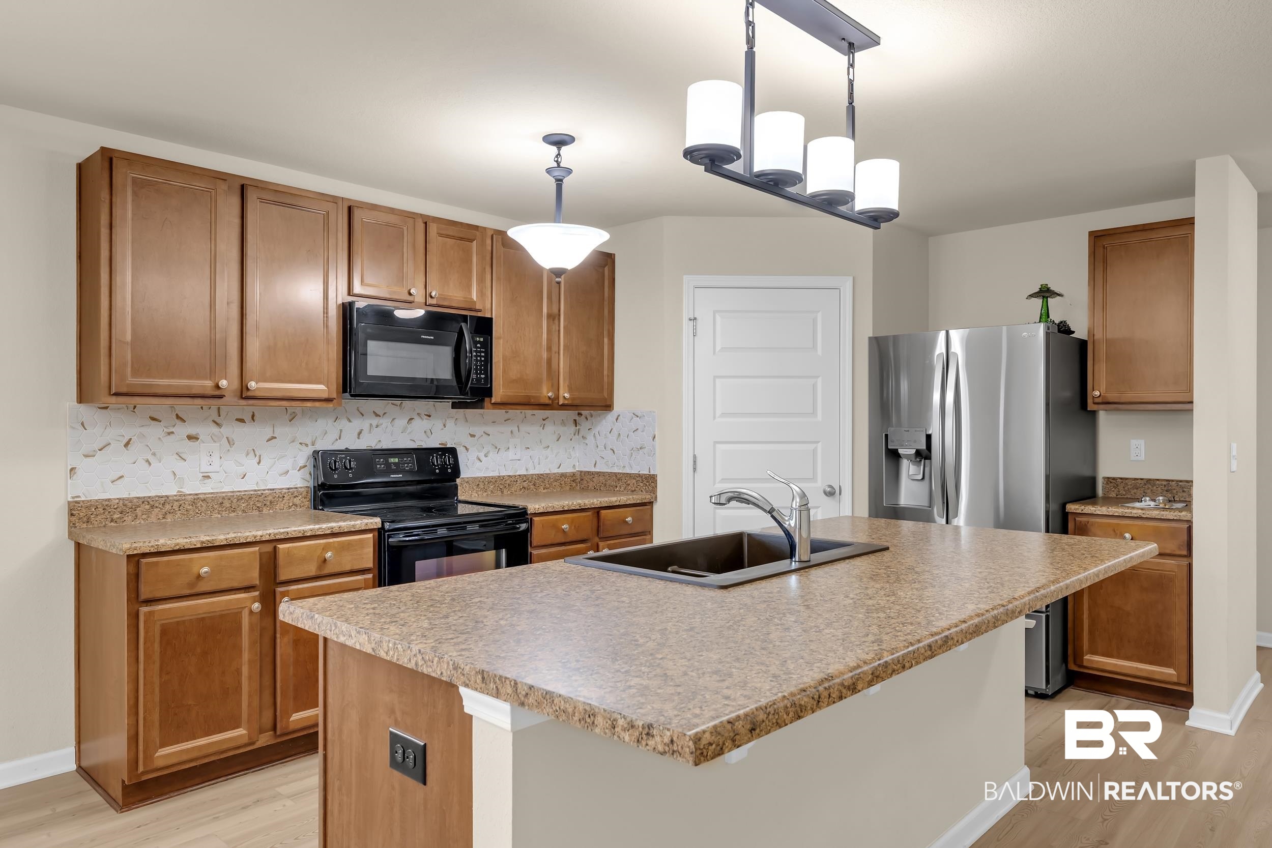 1704 Abbey Loop Foley, AL 36535 - Photo 12 of 38 Kitchen featuring a central island with an undermount sink, a linear pendant light fixture, wood-finish cabinetry, black appliances, and light-colored flooring