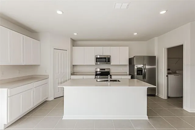 a large kitchen with stainless steel appliances a sink a stove a refrigerator a center island and cabinets