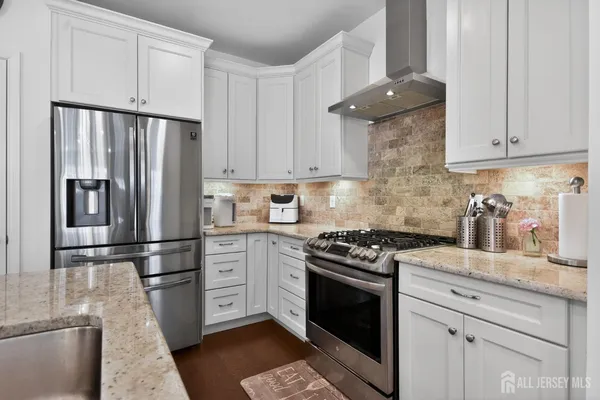 a kitchen with granite countertop a refrigerator stove and white cabinets
