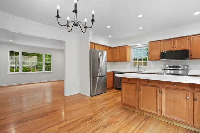 a kitchen with stainless steel appliances granite countertop a refrigerator a sink dishwasher a stove and a dining table with wooden floor