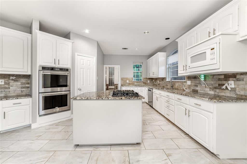 5801 Yeary Road Plano, TX 75093 - Photo 12 of 33 Spacious kitchen featuring an island with a gas cooktop, granite countertops, tile backsplash, white cabinetry, and stainless steel double ovens