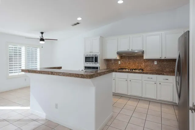 a kitchen with granite countertop white cabinets white appliances a sink and a window