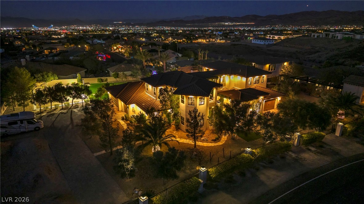 1158 Christian Road Henderson, NV 89002 - Photo 3 of 71 This captivating aerial view showcases a grand residence illuminated against a distant city skyline.