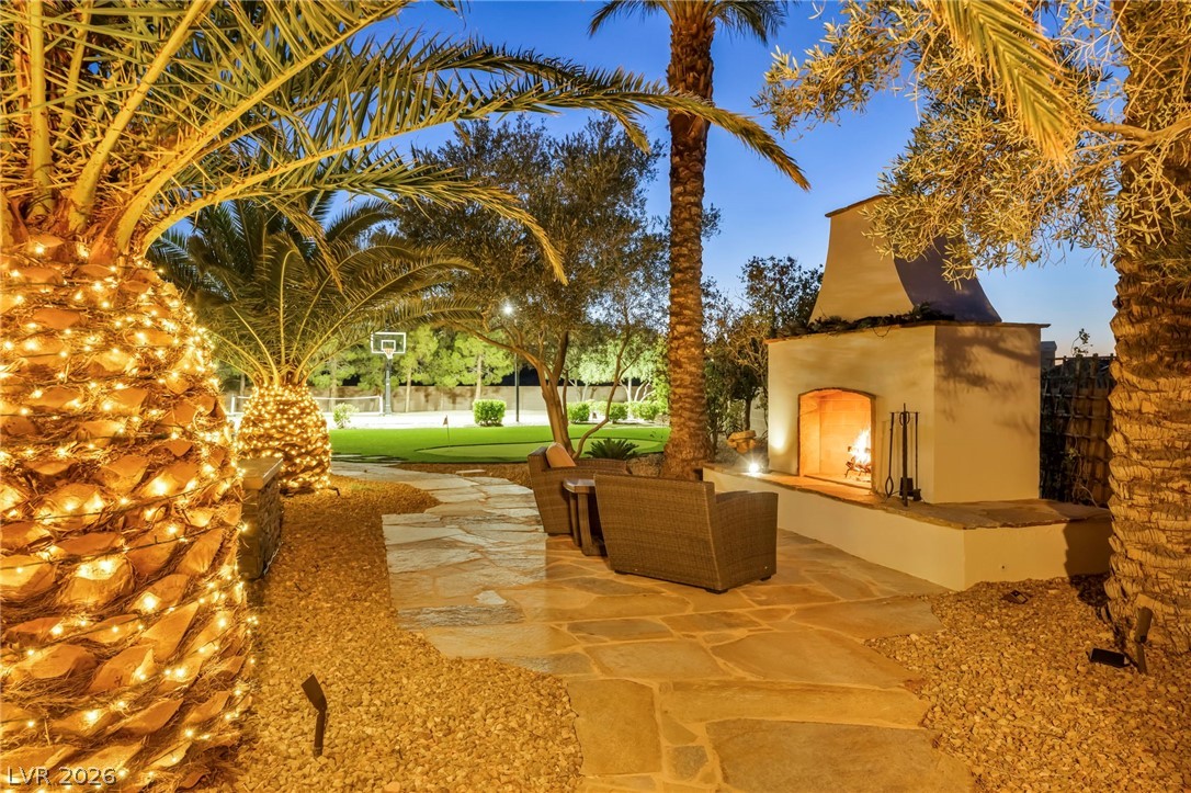 1158 Christian Road Henderson, NV 89002 - Photo 59 of 71 This inviting outdoor space features a fireplace and lush landscaping under a clear evening sky.