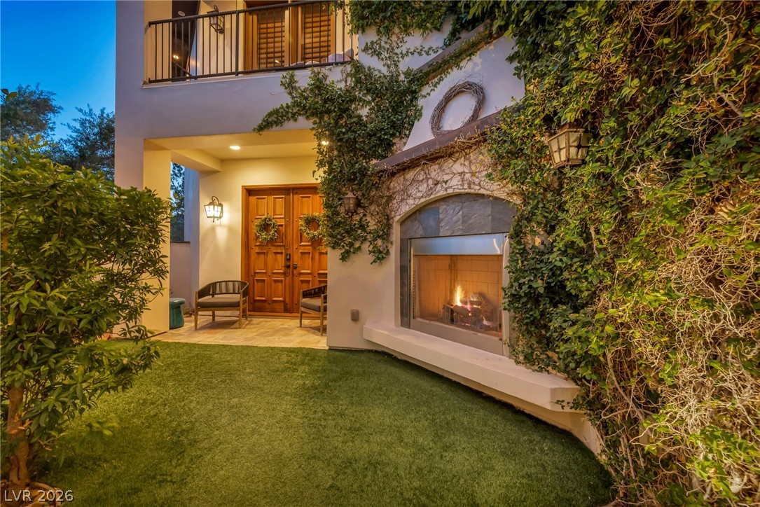 1158 Christian Road Henderson, NV 89002 - Photo 6 of 71 This inviting outdoor space features lush greenery, a cozy fireplace, and a welcoming entrance.