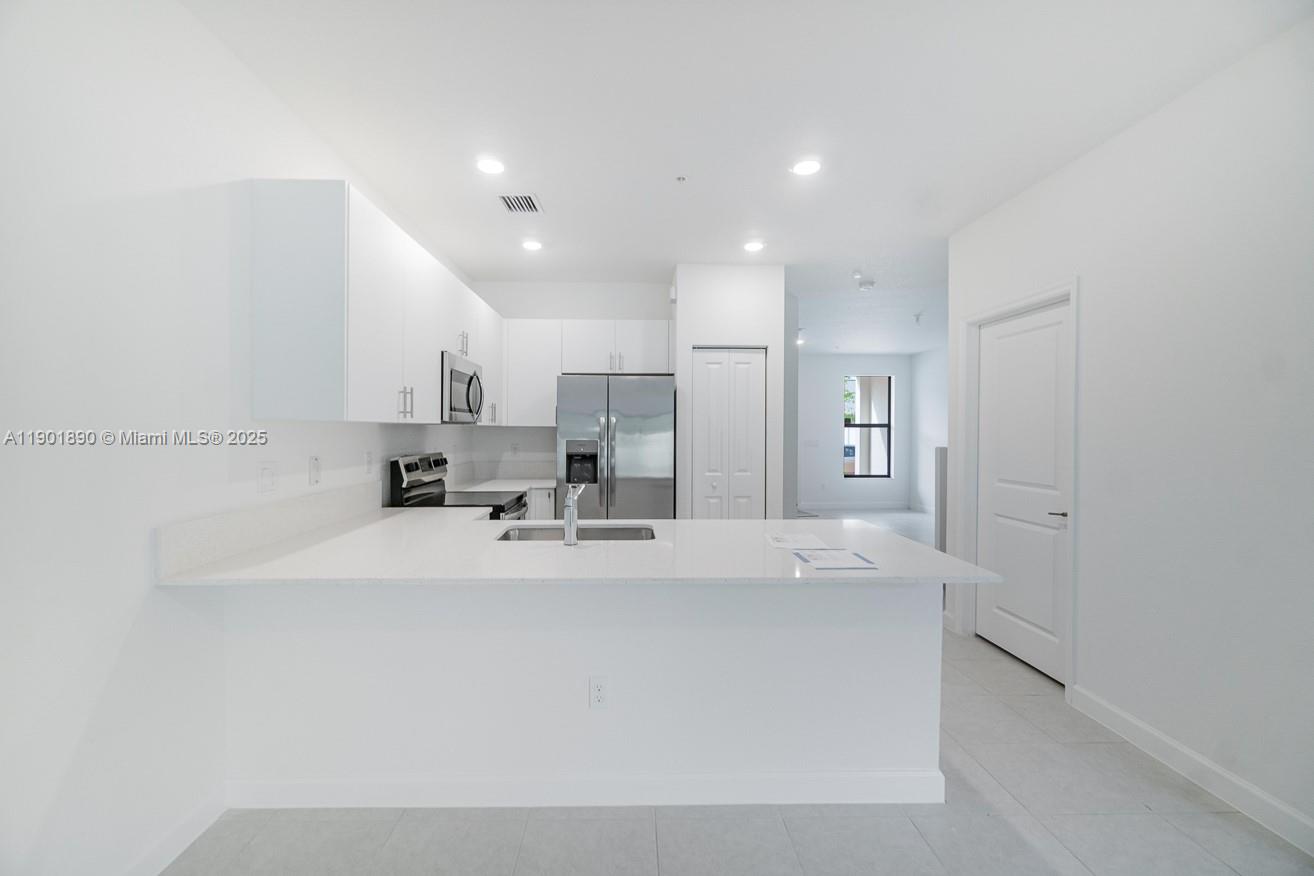 207 Southwest 159th Terrace Pembroke Pines, FL 33027 - Photo 11 of 37 a large white kitchen with kitchen island white cabinets and stainless steel appliances