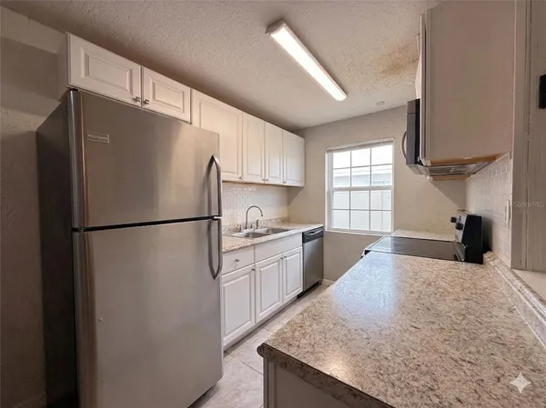 a kitchen with granite countertop a refrigerator a sink dishwasher a stove a washer and dryer with wooden floor