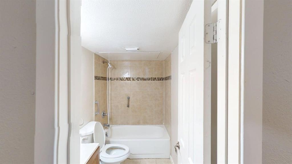 8110 Skillman Street, Unit 1016 Dallas, TX 75231 - Photo 9 of 12 Bathroom with a white bathtub, beige tiled shower surround, decorative mosaic tile accent, and a grab bar