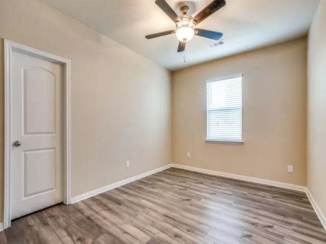 an empty room with wooden floor chandelier fan and windows