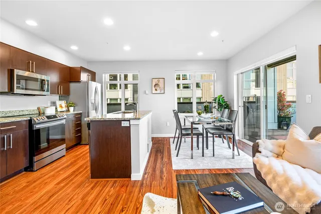 a living room with stainless steel appliances furniture wooden floor and a kitchen view