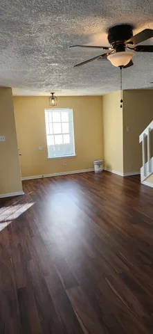 an empty room with wooden floor chandelier fan and windows