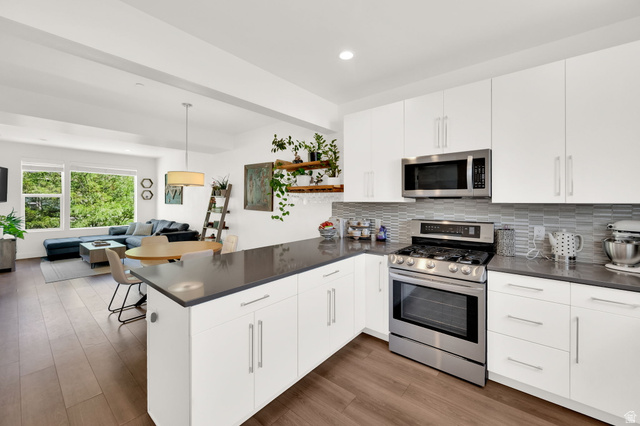 7713 Navarro View Court Midvale, UT 84047 - Photo 10 of 41 Modern kitchen featuring white cabinetry, stainless steel appliances, dark countertops, and a tiled backsplash