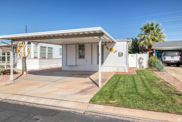 2990 East Riverside Drive, Unit 173 St. George, UT 84790 - Photo 32 of 38 White exterior with siding, featuring a covered carport, concrete driveway, and a small lawn area