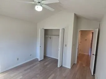 a view of an empty room with wooden floor and a ceiling fan