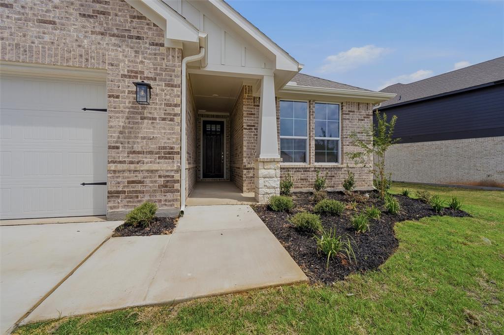 1201 Colca Drive Springtown, TX 76082 - Photo 5 of 32 Brick exterior with stone accents, covered front entry, attached garage with decorative hardware, and mature landscaping