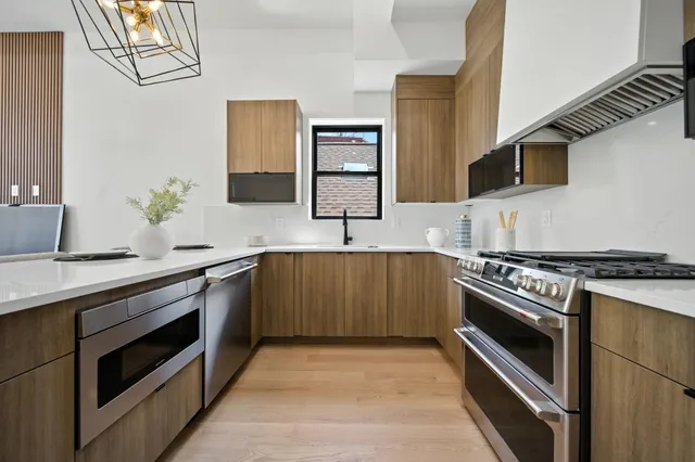 a large kitchen with stainless steel appliances a sink dishwasher a stove and a refrigerator with wooden floor