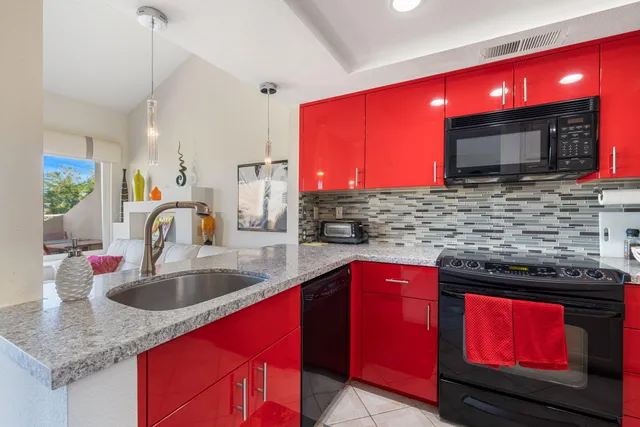 a kitchen with stainless steel appliances granite countertop a red stove top oven a sink with granite countertops and a flat screen tv