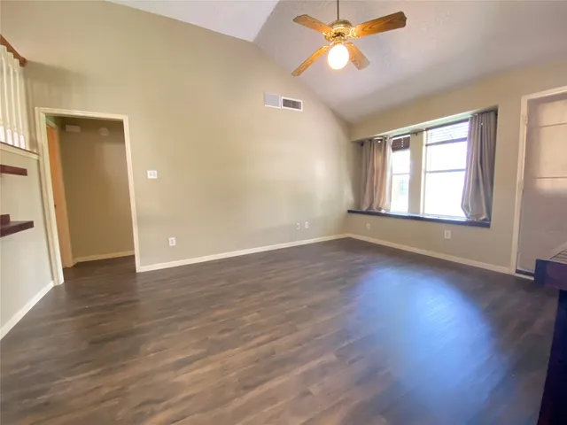 an empty room with wooden floor fan and windows
