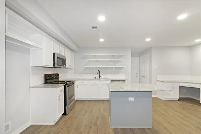 a kitchen with stainless steel appliances granite countertop a stove top oven a sink dishwasher and a refrigerator with wooden floor