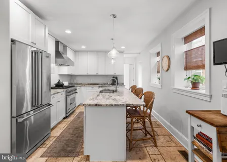 a kitchen with granite countertop a refrigerator a sink a stove and chairs
