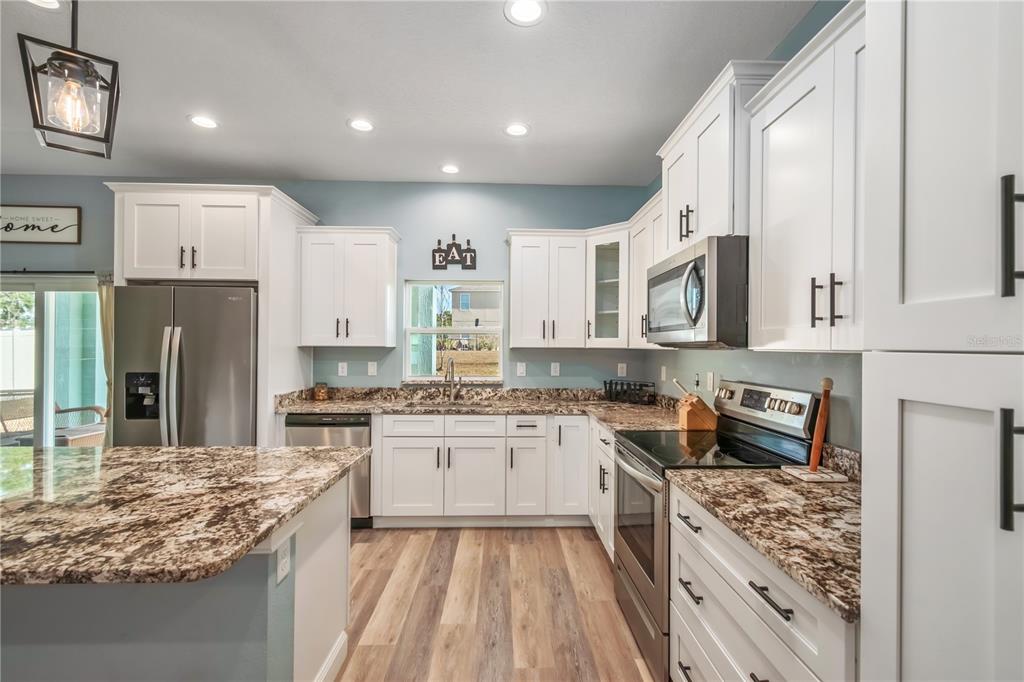 2839 Northeast 43rd Road Ocala, FL 34470 - Photo 21 of 50 a kitchen with stainless steel appliances granite countertop a stove top oven a sink dishwasher a refrigerator and white cabinets with wooden floor