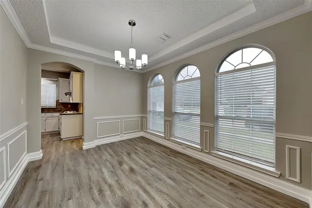 a view of a room with wooden floor chandeliers and kitchen view