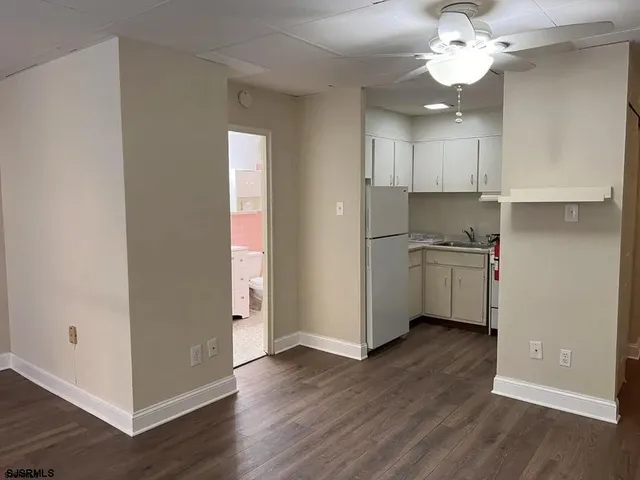 an empty room with wooden floor and a kitchen