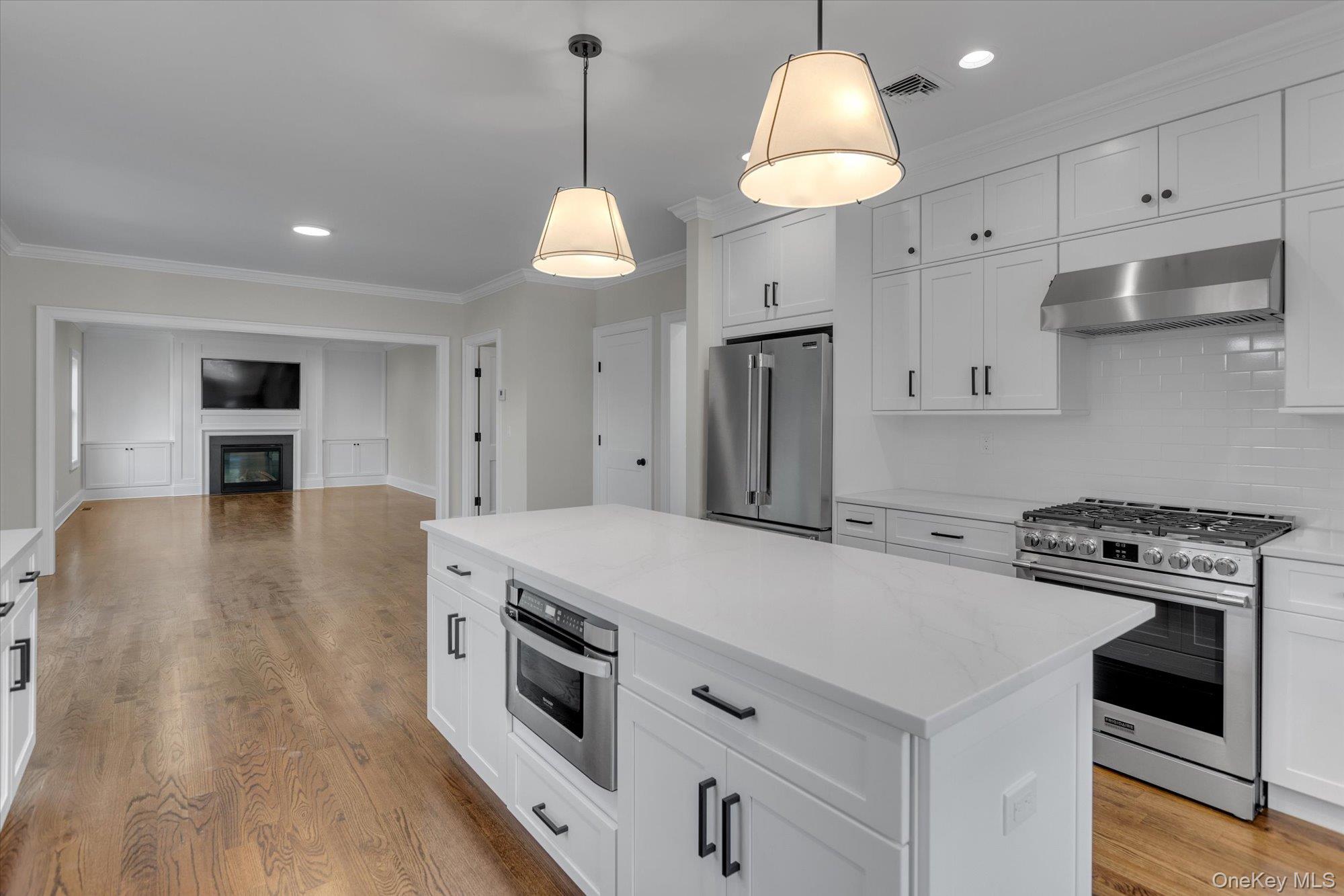 44 North Woodhull Road Huntington, NY 11743 - Photo 6 of 26 Kitchen featuring stainless steel appliances, a center island, ornamental molding, white cabinets, and wall chimney range hood