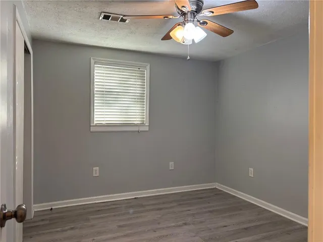 an empty room with wooden floor fan and windows