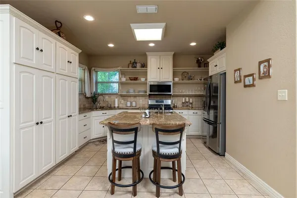 a kitchen with stainless steel appliances kitchen island granite countertop a refrigerator oven a sink dishwasher and white cabinets with wooden floor