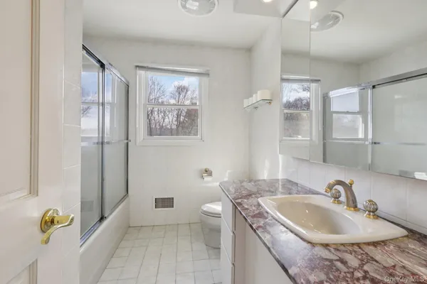 a bathroom with a granite countertop sink a toilet a mirror and shower
