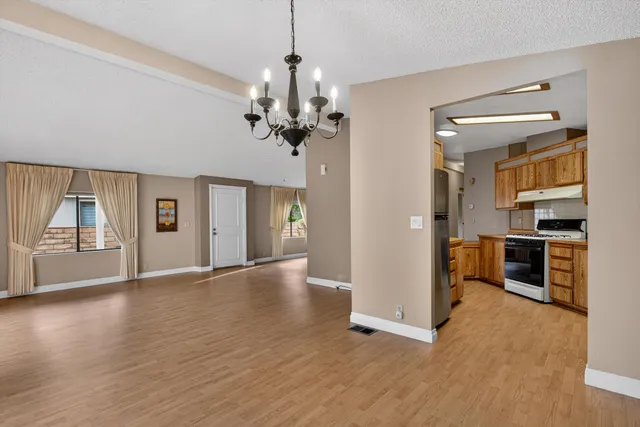an empty room with wooden floor kitchen view and a window