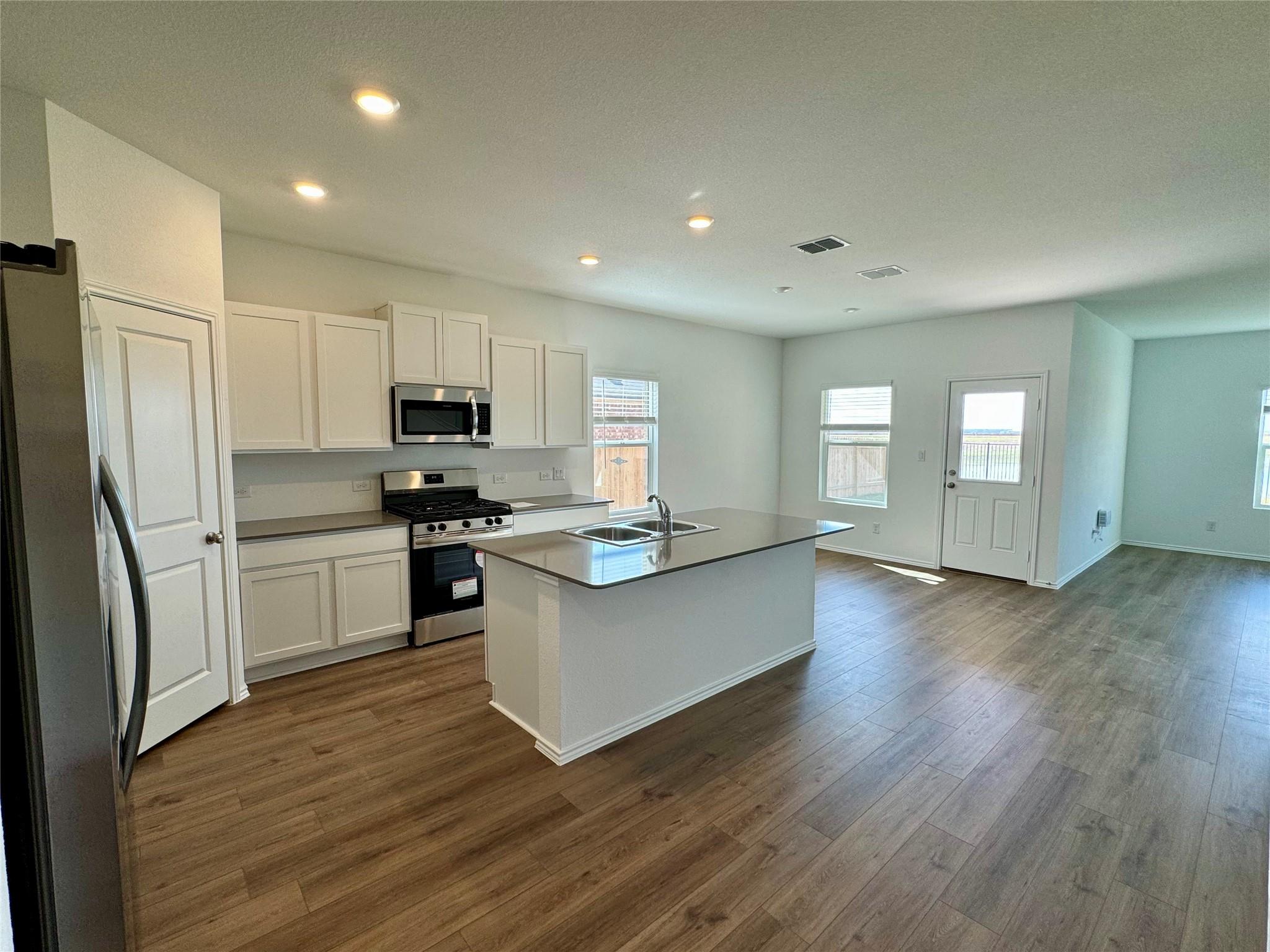 134 Agua Azul Bend Kyle, TX 78640 - Photo 2 of 10 Kitchen with stainless steel appliances, white cabinetry, an island with sink, dark wood-style floors, and recessed lighting