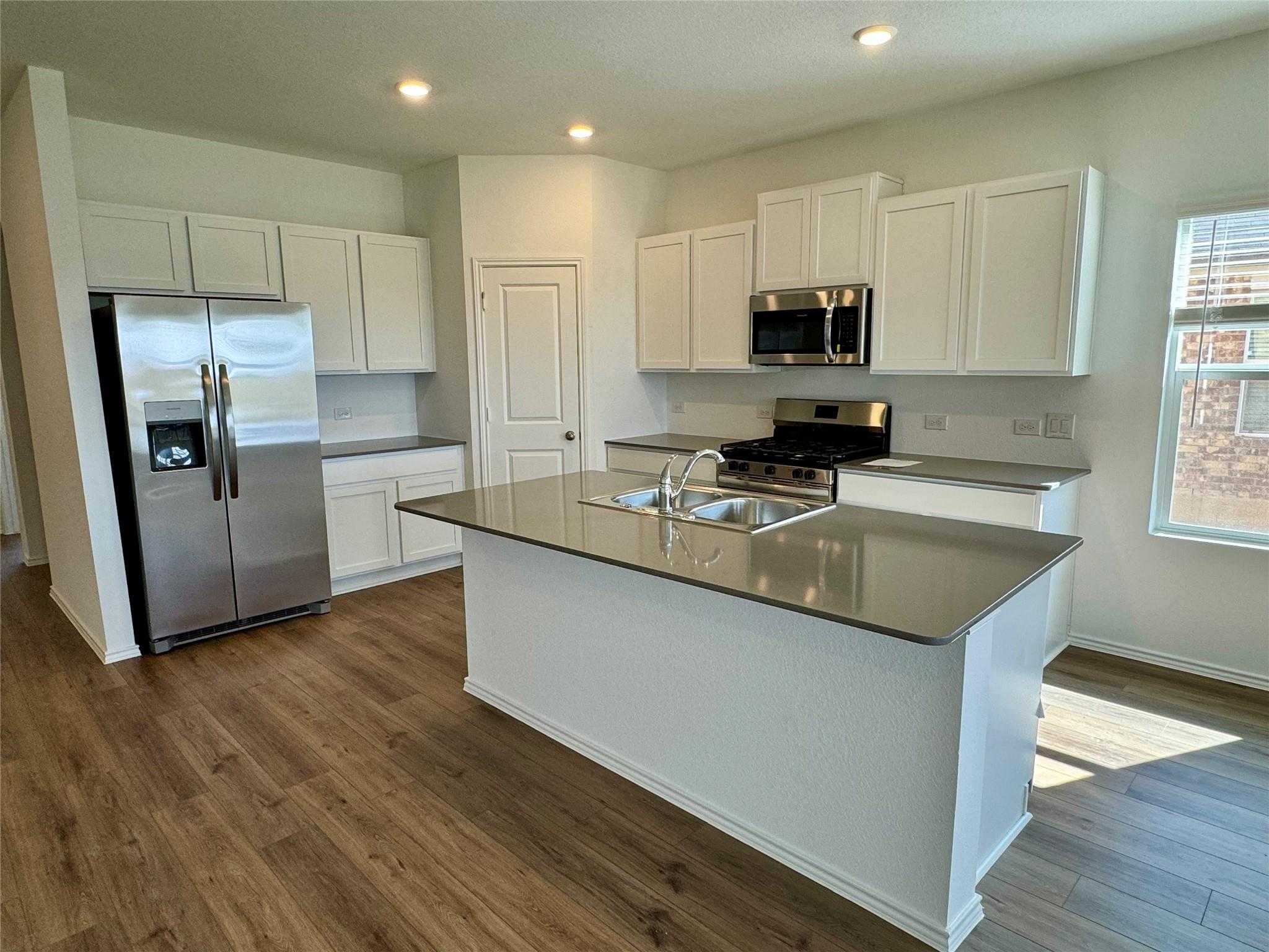 134 Agua Azul Bend Kyle, TX 78640 - Photo 3 of 10 Kitchen with white cabinets, stainless steel appliances, an island with sink, dark wood-style floors, and recessed lighting