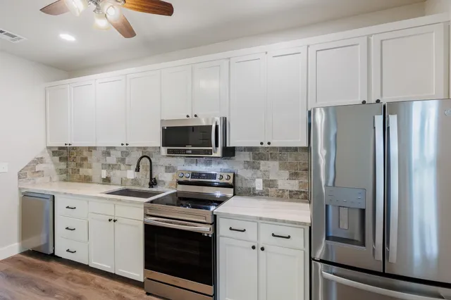 a kitchen with stainless steel appliances granite countertop a refrigerator a stove a sink and white cabinets with wooden floor