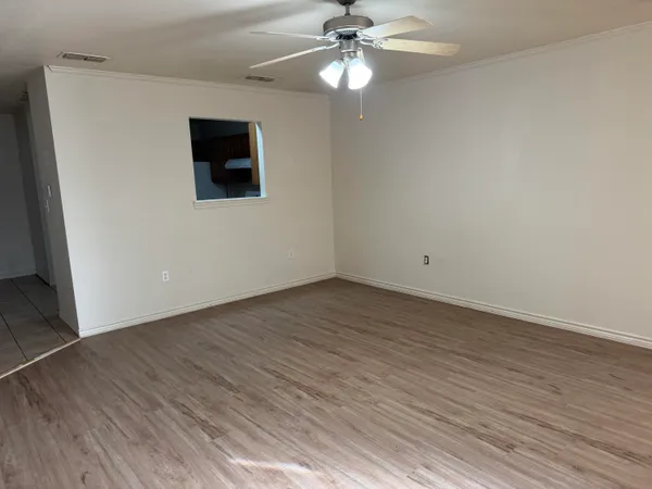 a view of an empty room with wooden floor and a ceiling fan