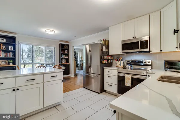 a kitchen with stainless steel appliances kitchen island granite countertop a refrigerator a stove a sink and white cabinets with wooden floor