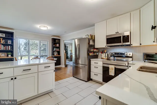 a kitchen with stainless steel appliances kitchen island granite countertop a refrigerator a stove a sink and white cabinets with wooden floor