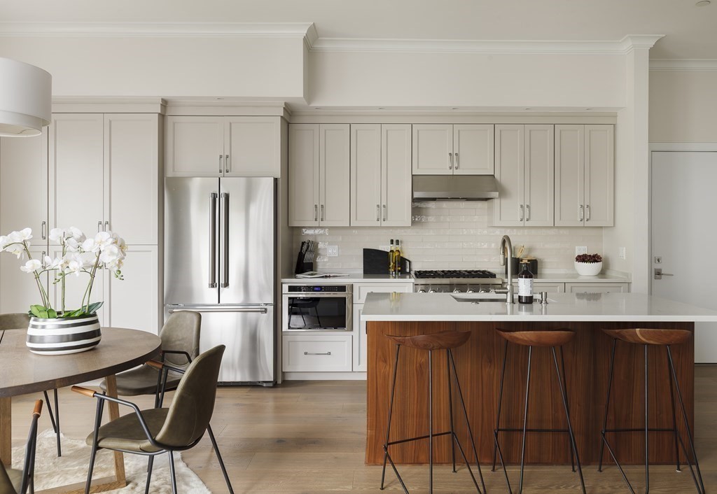 11 Tannery Brook Row, Unit 2 Somerville, MA 02144 - Photo 2 of 17 a kitchen with stainless steel appliances granite countertop a refrigerator a stove a sink and white cabinets with wooden chairs