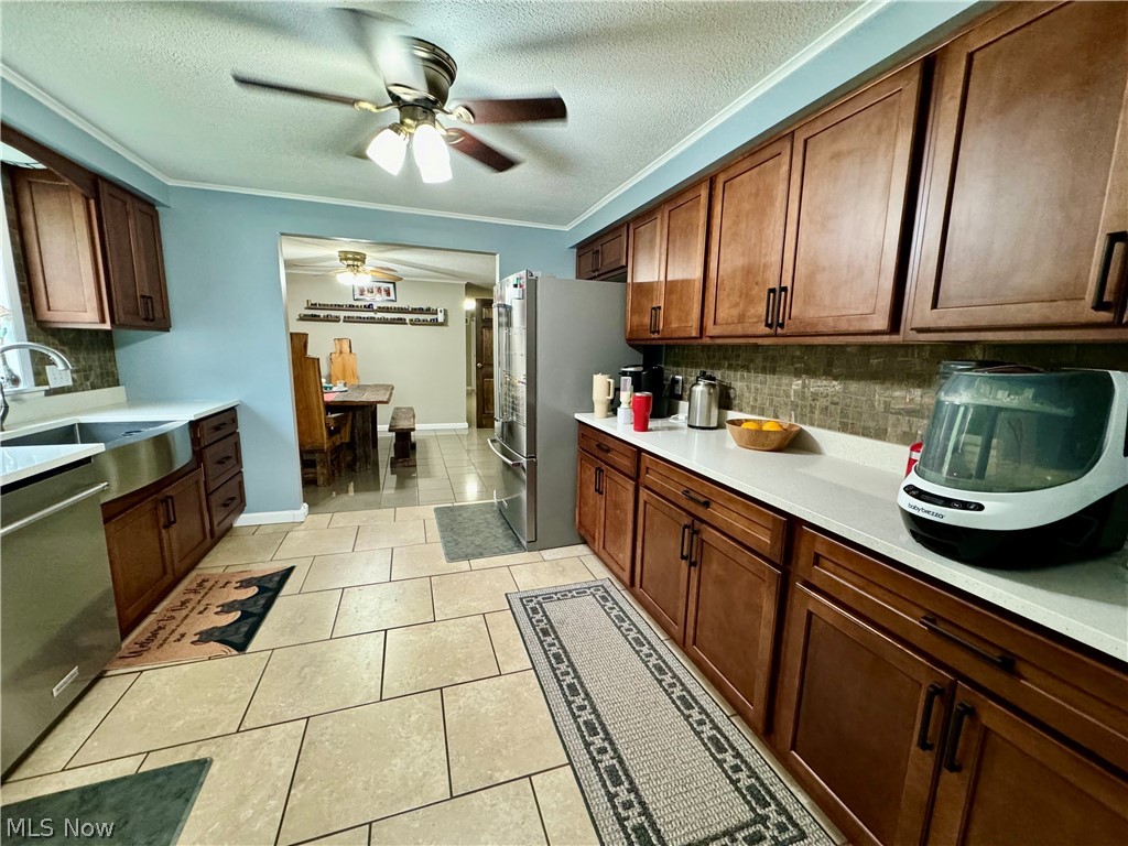 86 Cunningham Hill Road Harrisville, WV 26362 - Photo 11 of 32 Kitchen featuring light tile patterned floors, ceiling fan, appliances with stainless steel finishes, decorative backsplash, and ornamental molding
