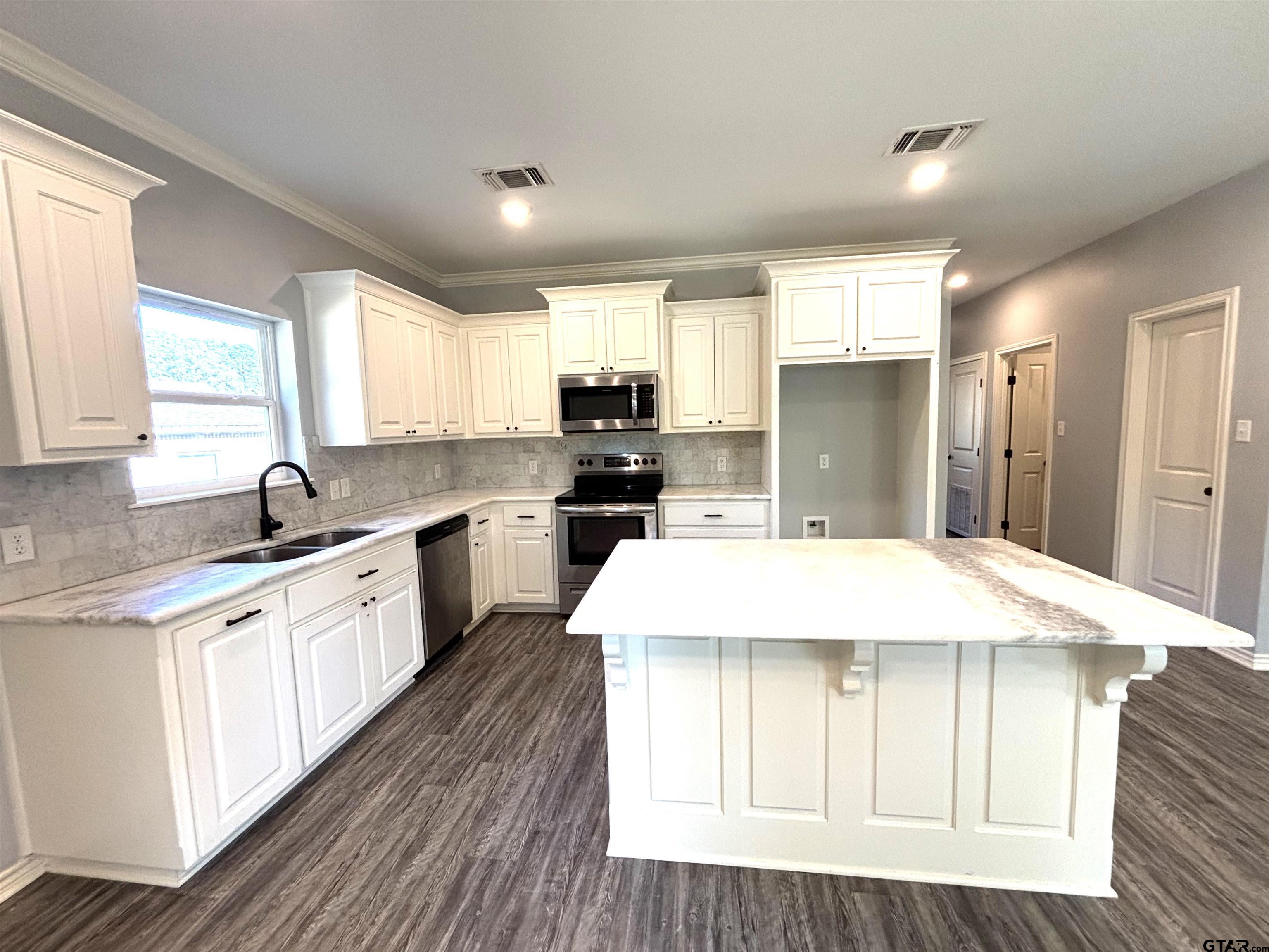 196 Twisted Oaks Road Rusk, TX 75785 - Photo 3 of 25 a large kitchen with kitchen island granite countertop a stove a sink a refrigerator and white cabinets with wooden floor