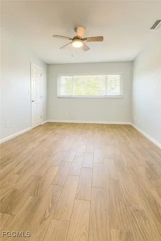 an empty room with wooden floor chandelier fan and windows