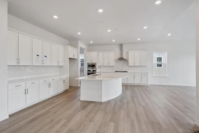 a large kitchen with white cabinets a sink dishwasher a dining table and chairs with wooden floors