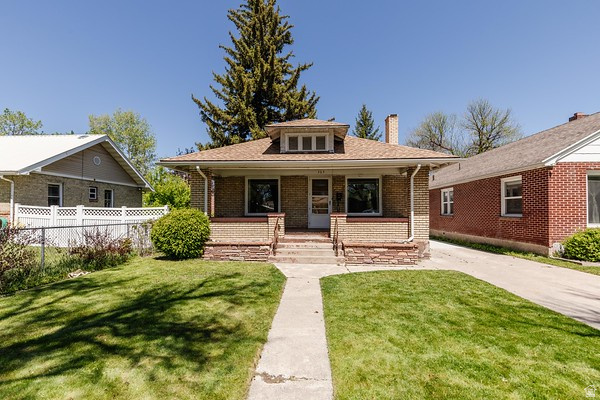 365 West 200 North Logan, UT 84321 - Photo 43 of 45 Brick facade residence with a covered porch, stone foundation accents, a concrete walkway, a paved driveway, and a front lawn