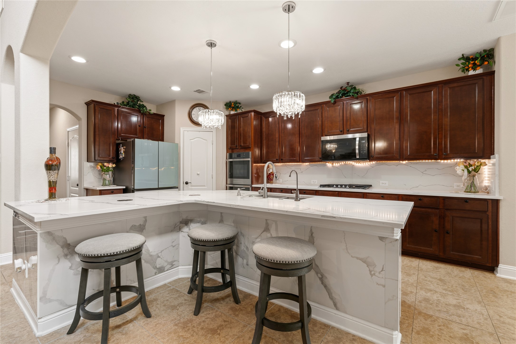 5802 Layton Meadows Lane Spring, TX 77379 - Photo 12 of 42 Kitchen hero shot. Full L-shaped island with marble sides, three bar stools, dual crystal chandeliers, stainless appliances, and full cabinet wall.