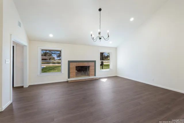 a view of an empty room with wooden floor fireplace and a window