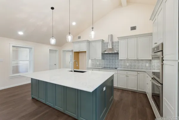 a kitchen with a sink a stove a oven and white cabinets
